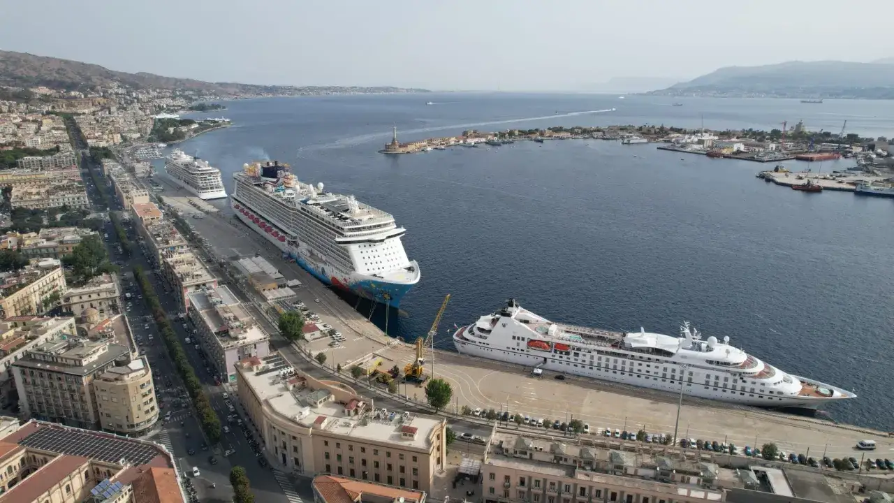 Il terminal crociere di Messina accoglie navi imponenti. La città si estende lungo la costa, con il mare blu sullo sfondo.