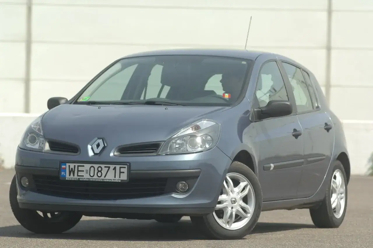 Szary Renault Clio 3 z widocznymi przednimi żarówkami, zaparkowany na zewnątrz.