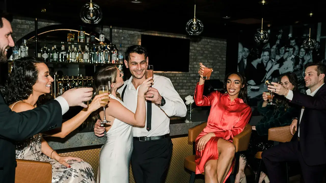 Feiernde Menschen sto&szlig;en mit Cocktails an. Der Dresscode ist cocktail casual, die Stimmung ausgelassen.