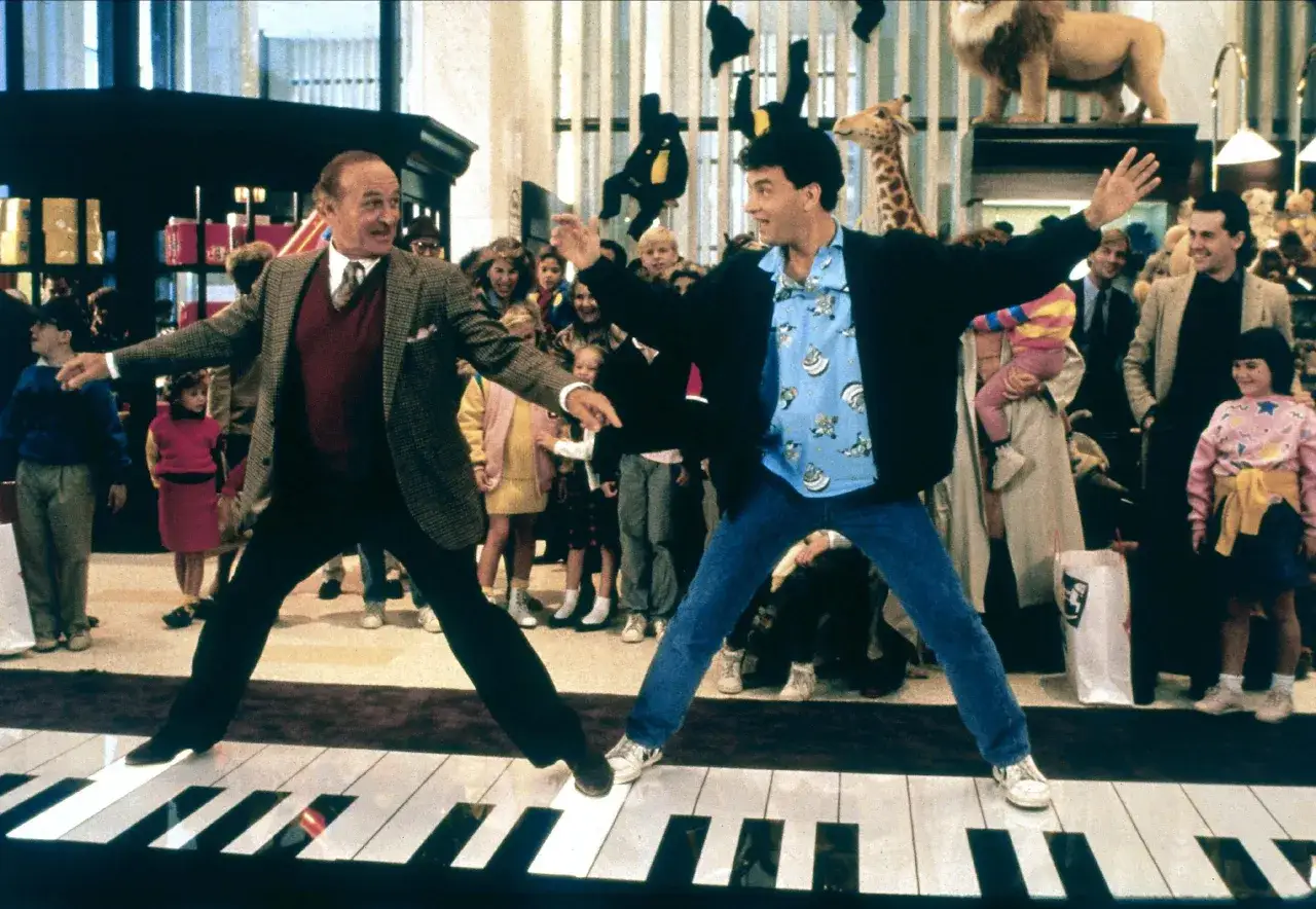 Un uomo e un bambino ballano su un enorme pianoforte in un negozio di giocattoli, una scena iconica di un film con un piano sequenza indimenticabile.