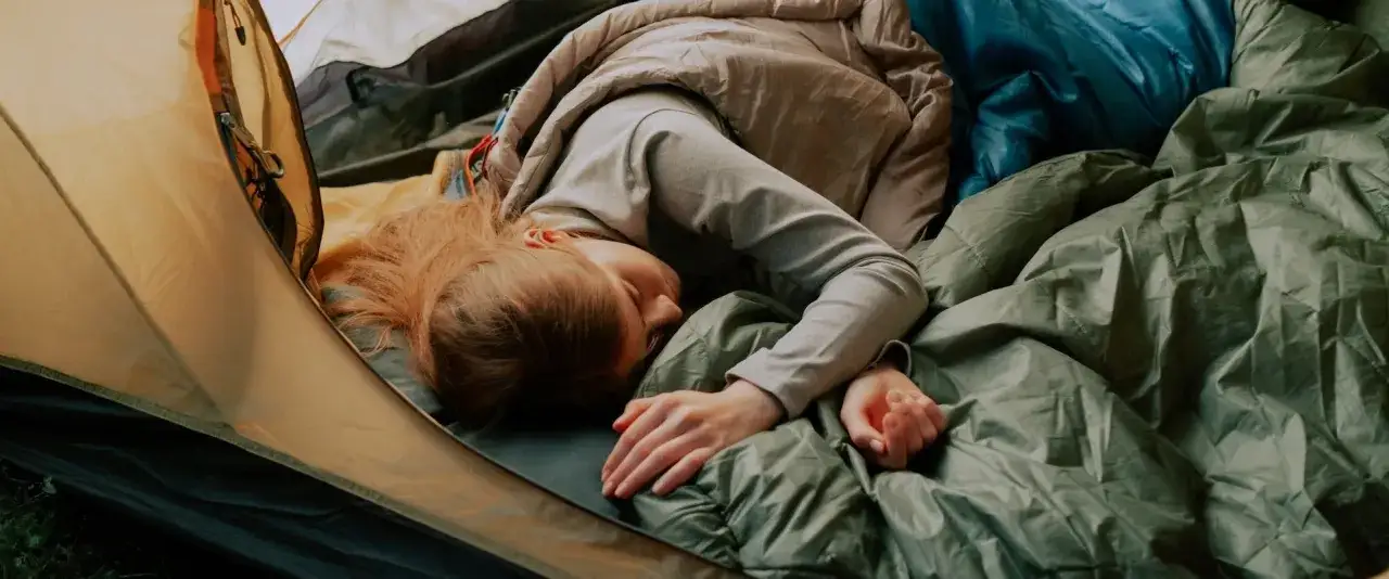 M&auml;dchen schl&auml;ft in einem Zelt auf einer Isomatte unter einer Luftmatratze, eingekuschelt in einen Schlafsack.