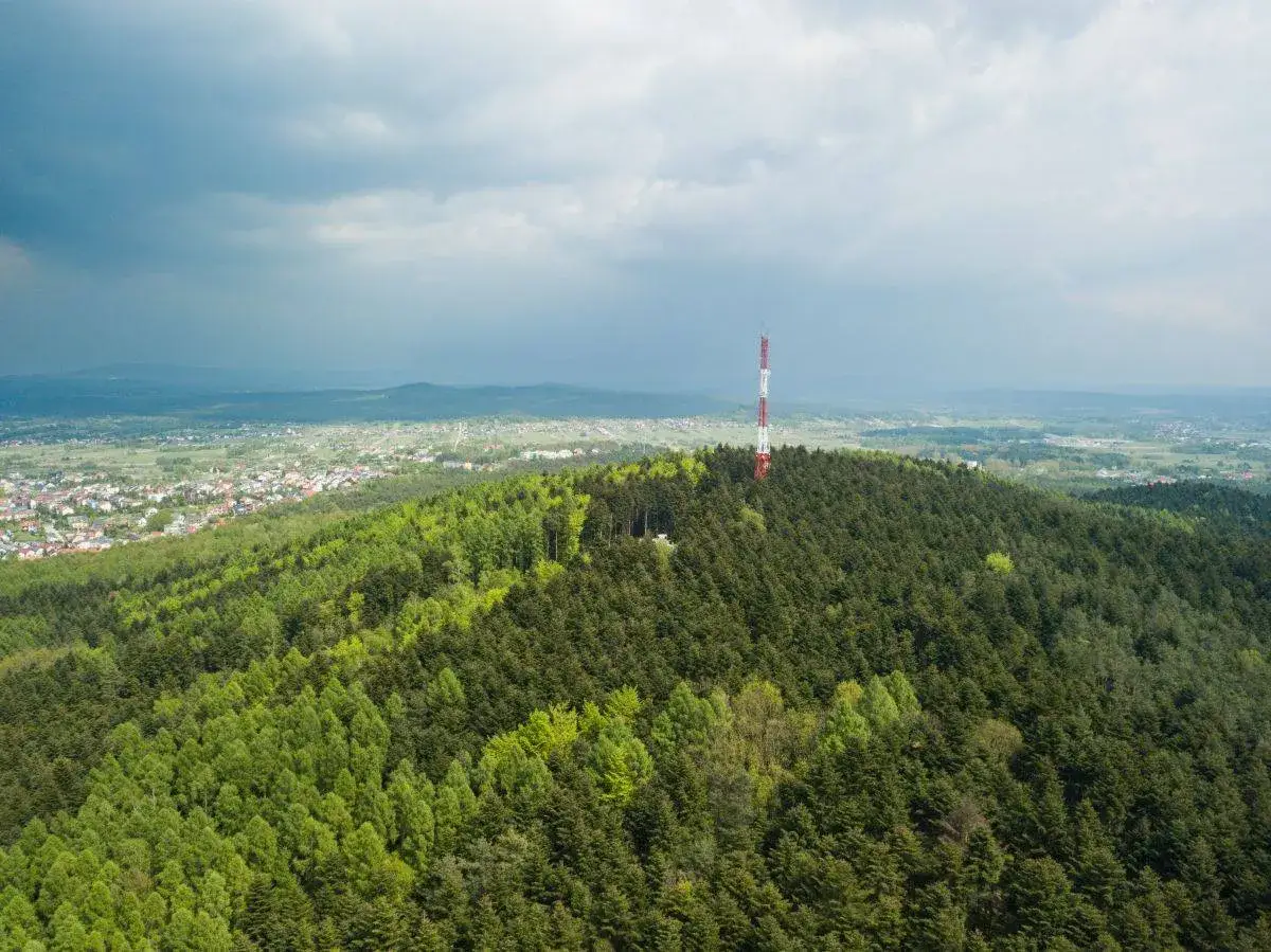 Wieża telekomunikacyjna na zalesionym wzgórzu, z widokiem na miasto. To pokazuje kielce wysokość nad poziomem morza.