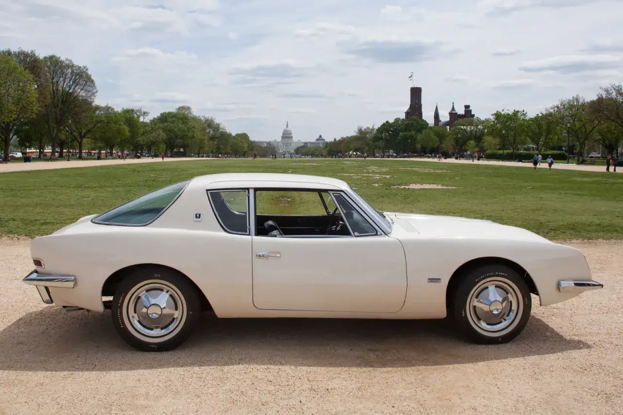 En vit Studebaker Avanti parkerad på grusväg med Capitolium i bakgrunden.