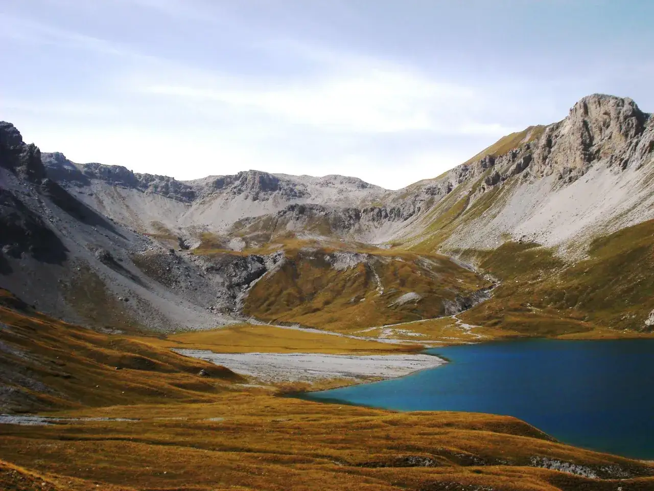 Ein tiefblauer Bergsee, der Lai da Rims, spiegelt die majestätischen, von Geröll bedeckten Gipfel wider.