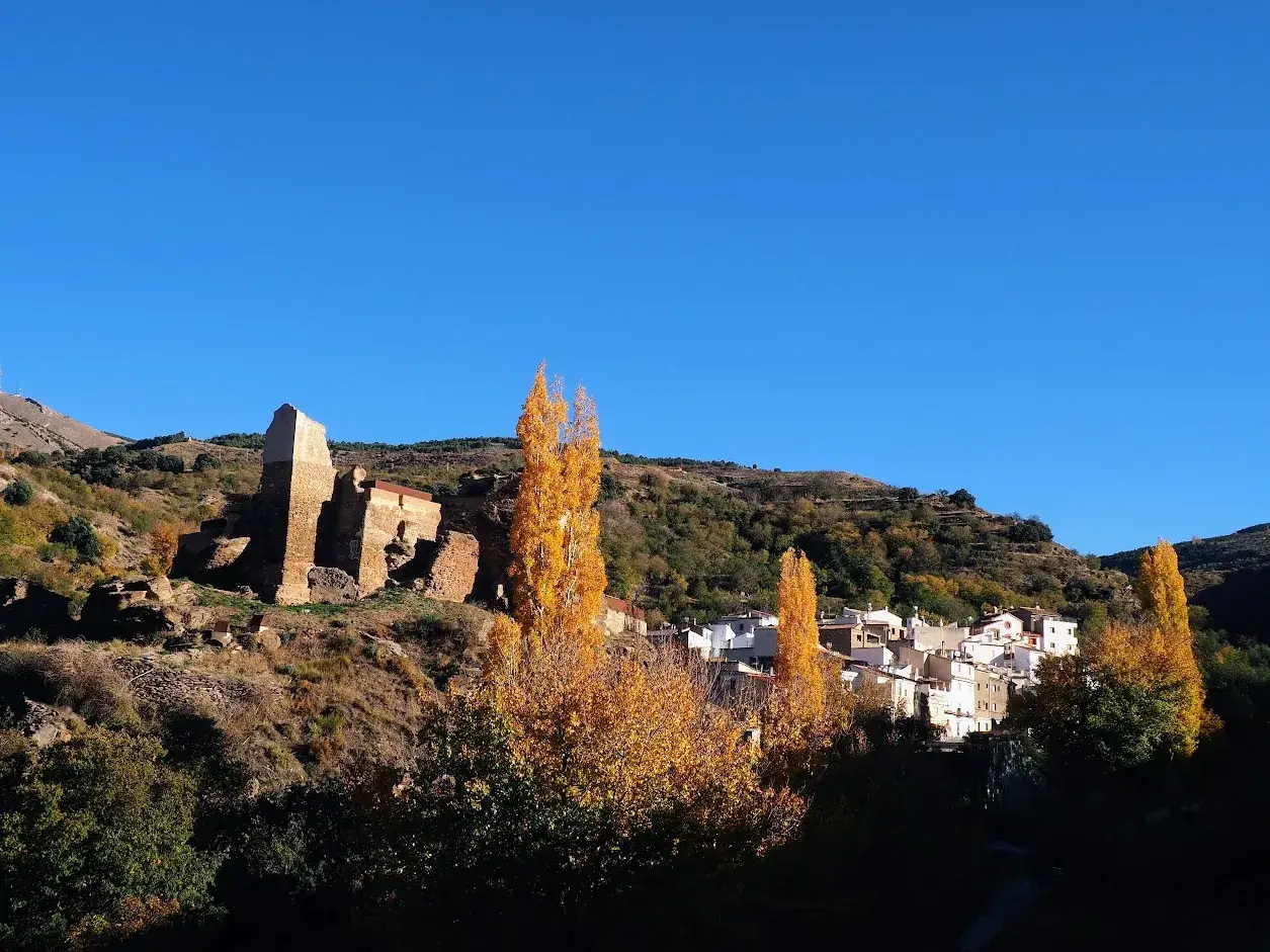 Ruinas y casas blancas en Bacares, rodeadas de árboles otoñales bajo un cielo azul. Un lugar con historia que ver.