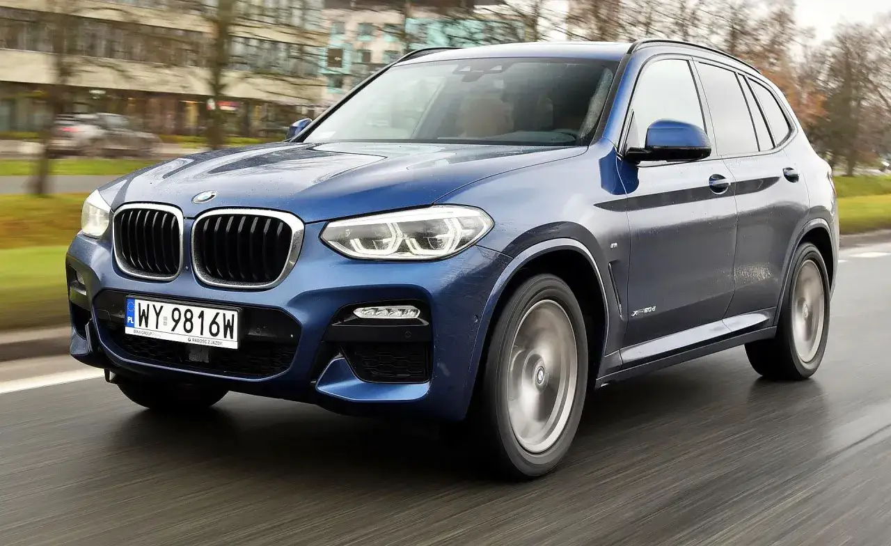 Niebieskie BMW G01 w ruchu, z widocznymi charakterystycznymi nerkami i reflektorami.