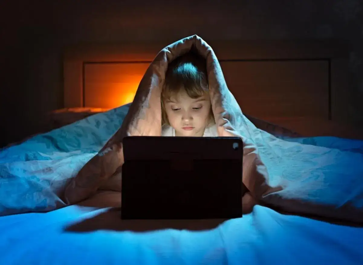 Un enfant de 2 ans, blotti sous une couverture, d&eacute;couvre un monde magique sur sa tablette.