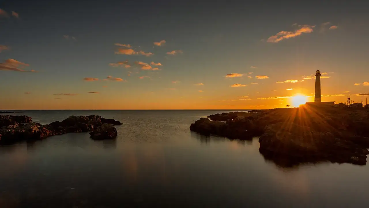 Fyren vid Campofelice di Roccella badar i solnedgångens gyllene ljus. Steniga klippor möter det lugna havet.