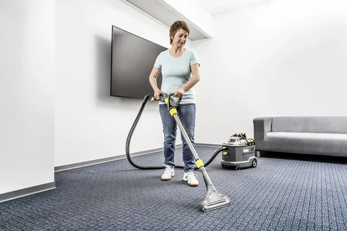 Une femme utilise un appareil pour le nettoyage moquette vapeur. Un canap&eacute; gris et un &eacute;cran plat sont visibles.