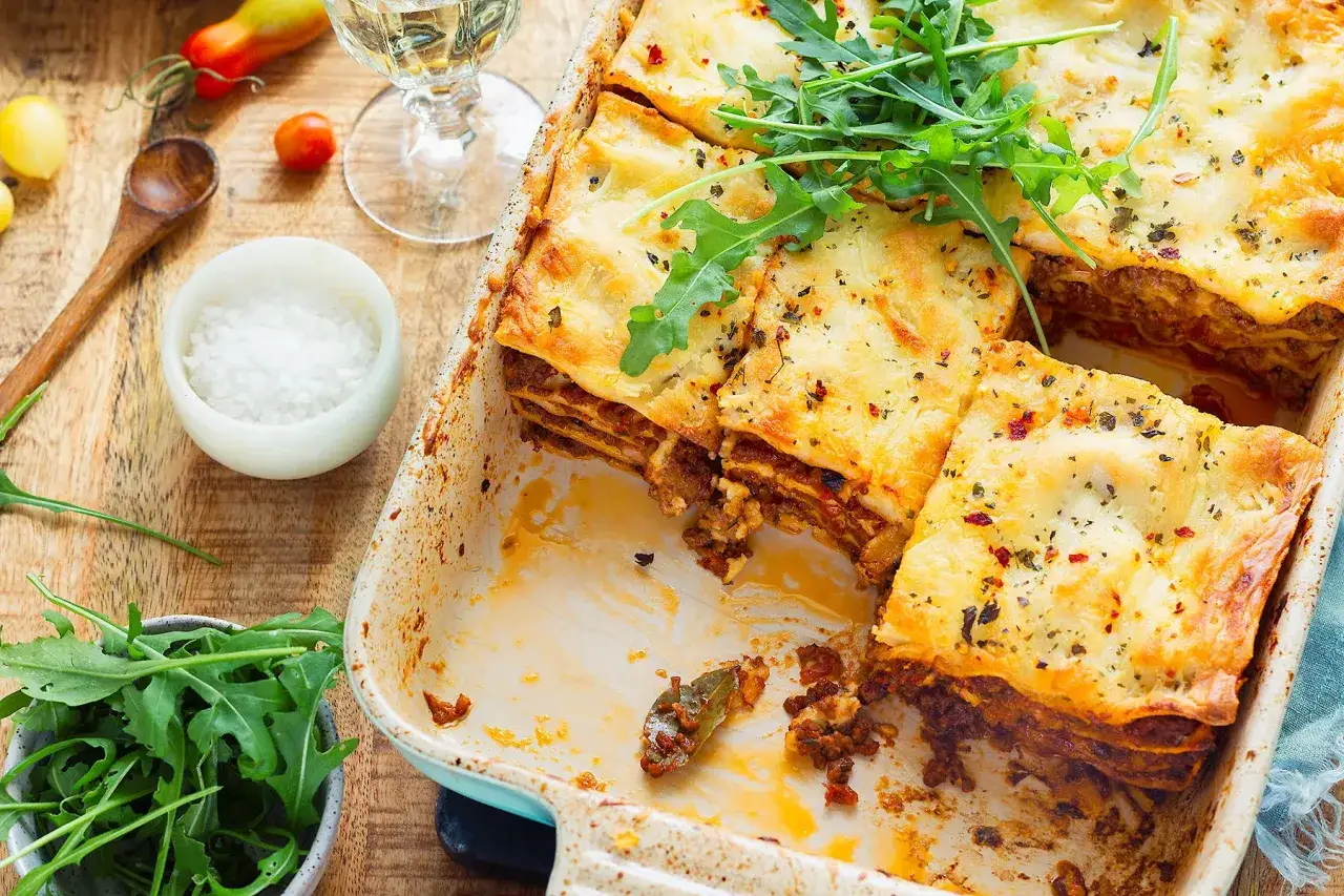 Pyszne, gorące danie, ile piec lasagne zostało już prawie zjedzone. Na wierzchu rukola, obok miseczka z solą i drewniana łyżka.