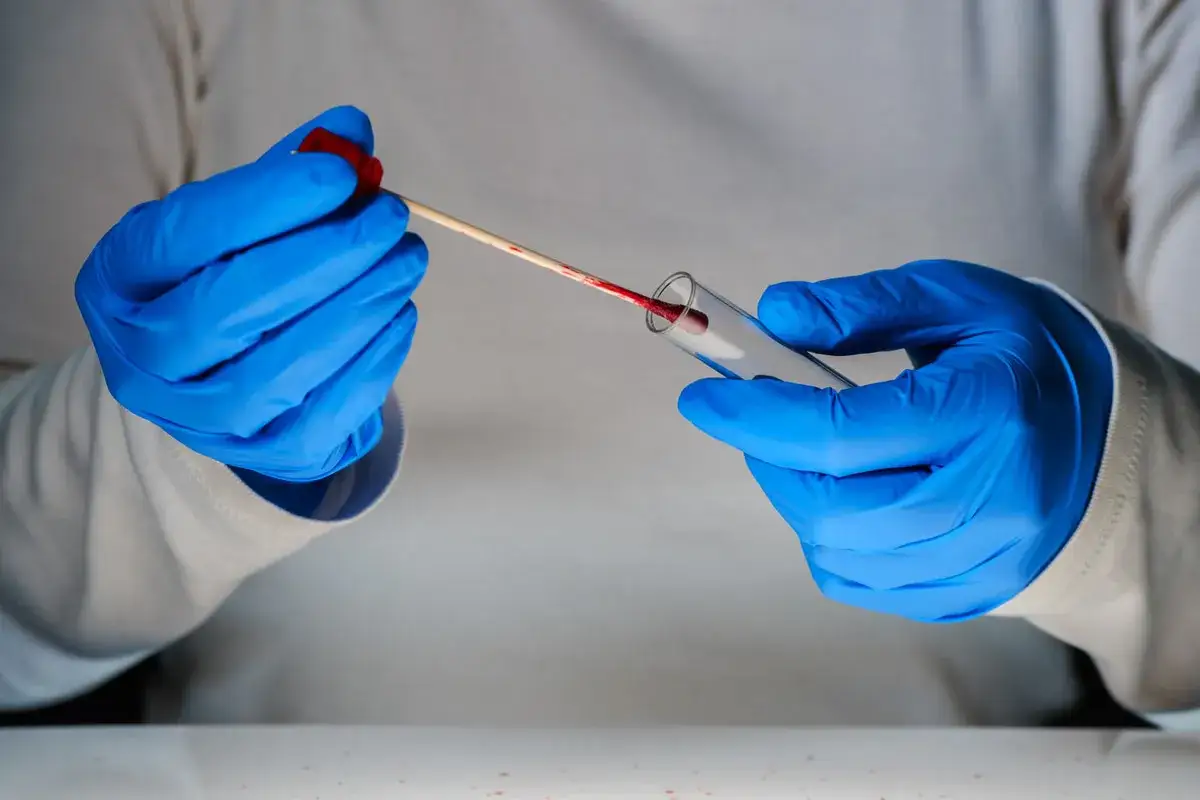 Ein Forensiker sammelt mit einem Tupfer eine Probe aus einem Reagenzglas.