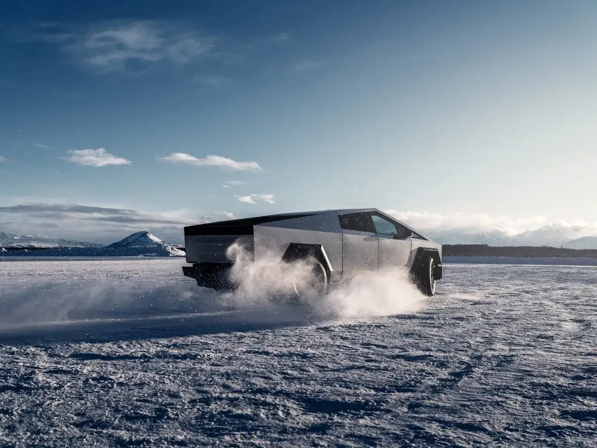 Tesla Cybertruck ile kosztuje? Futurystyczny pickup sunie po zaśnieżonej równinie, wzbijając tumany śniegu.