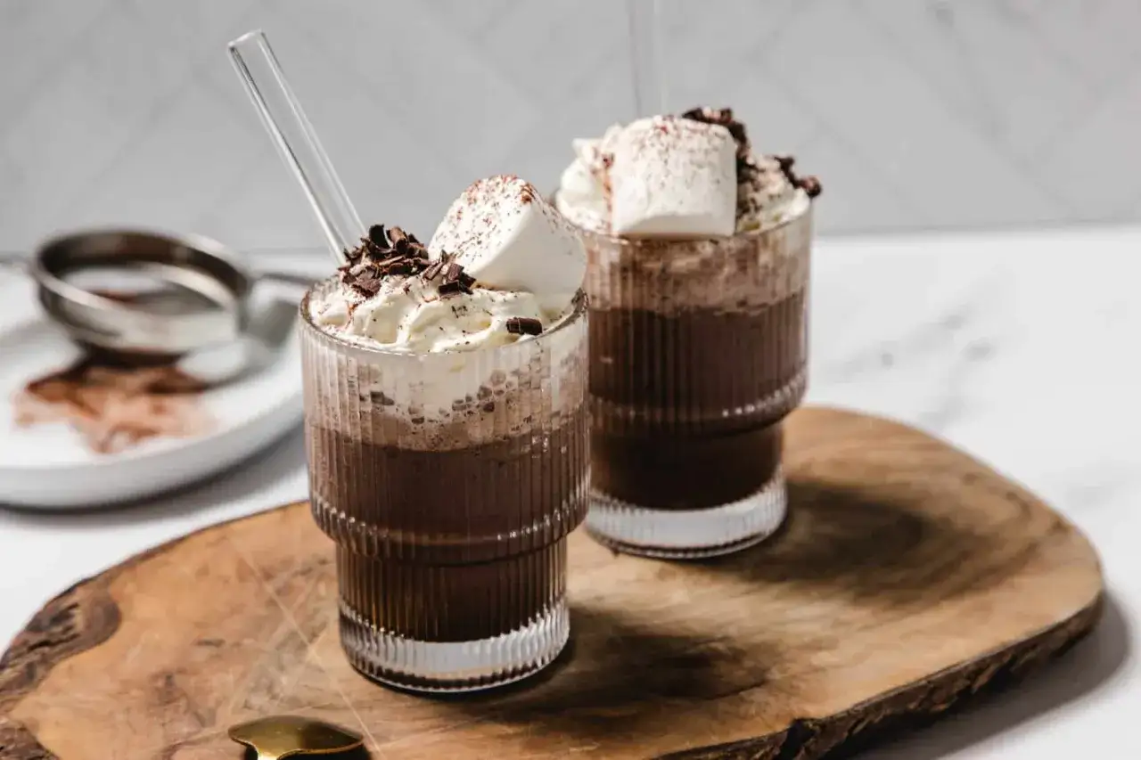 Två glas med varm choklad, toppad med vispgrädde, marshmallows och chokladspån. Perfekt för en mysig stund à la Kaffe Karlsson.