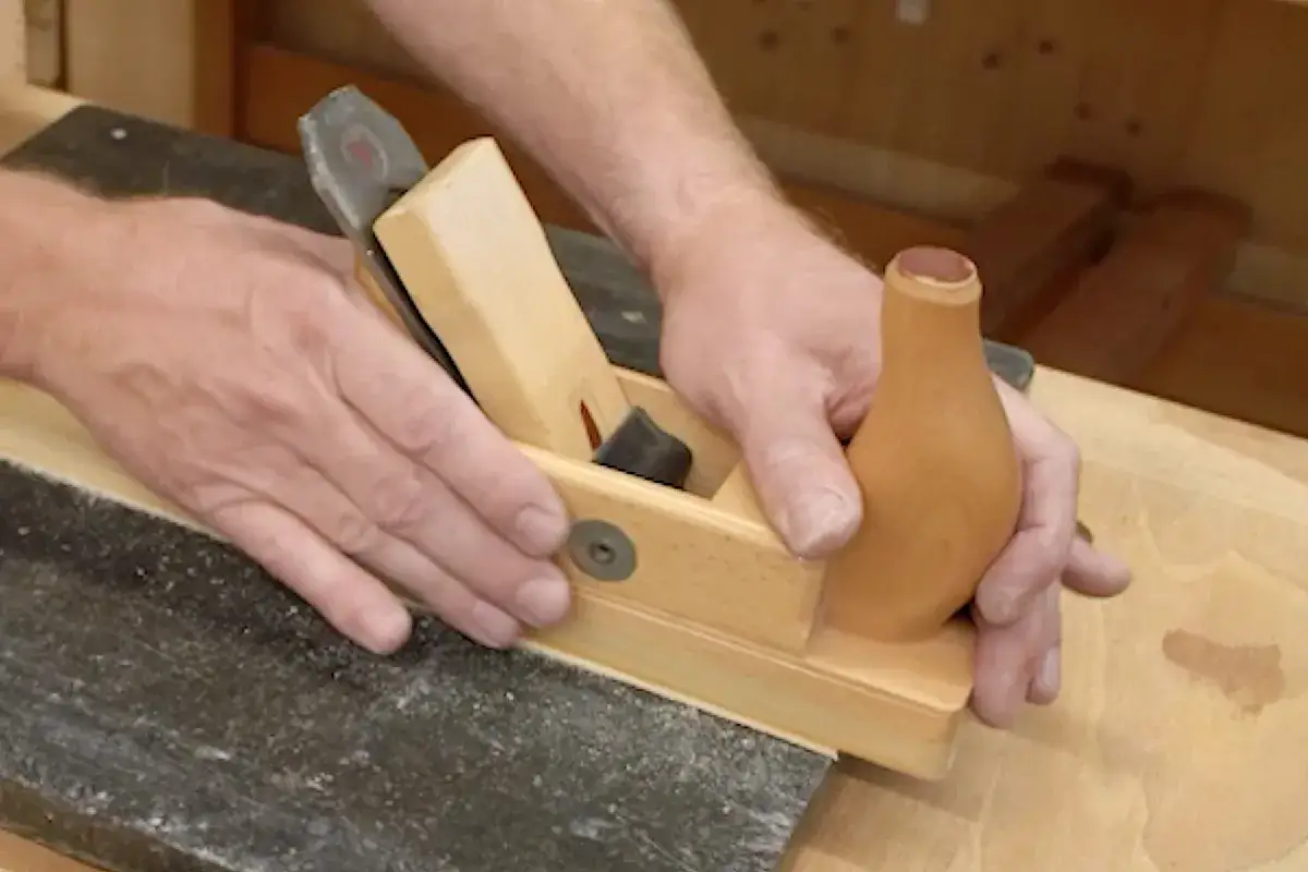 Main d'un artisan guidant un rabot en bois sur une planche. Apprenez comment utiliser un rabot électrique pour un travail du bois précis.