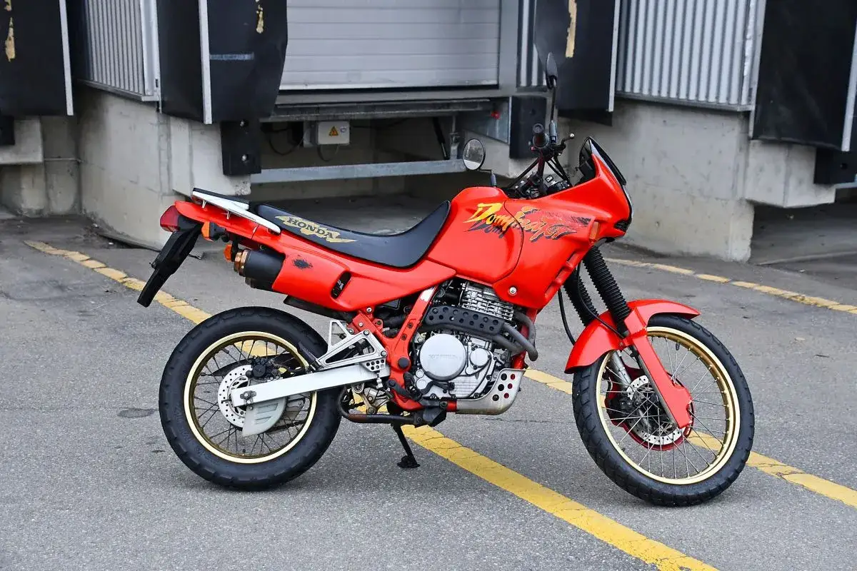 Czerwony motocykl Honda Dominator 650, gotowy na przygody. Wady i zalety tego klasyka do odkrycia.