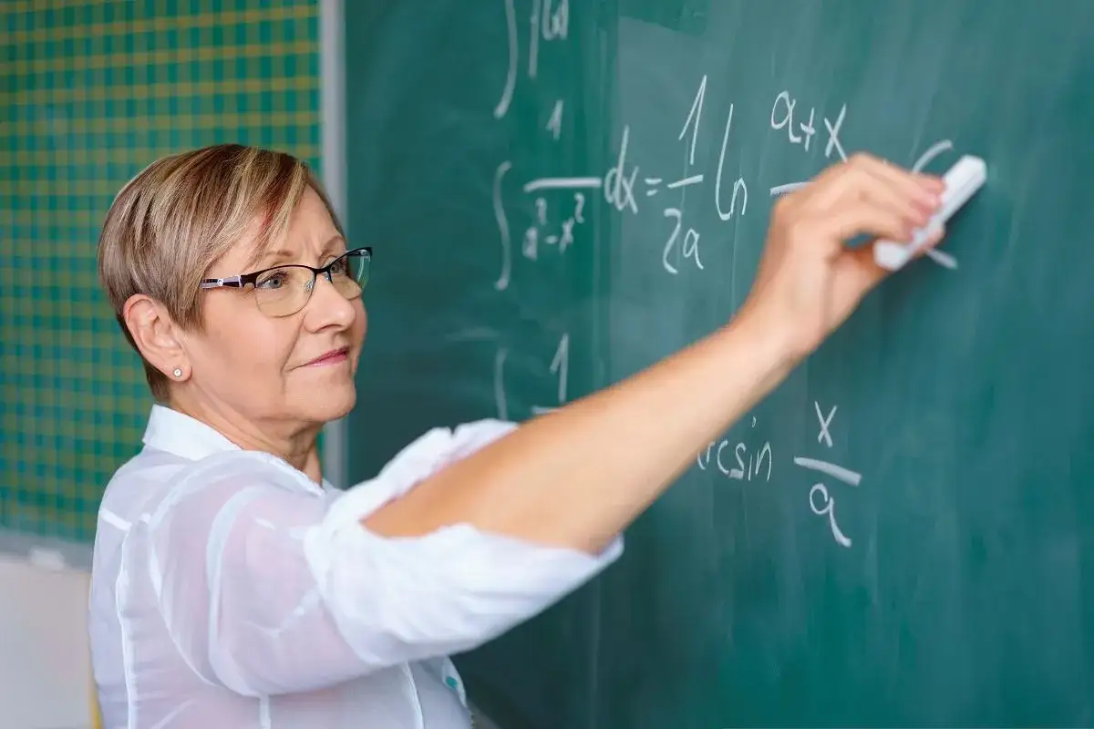 Nauczycielka matematyki pisze wzory na tablicy. Zastanawiasz się, ile zarabia nauczyciel?