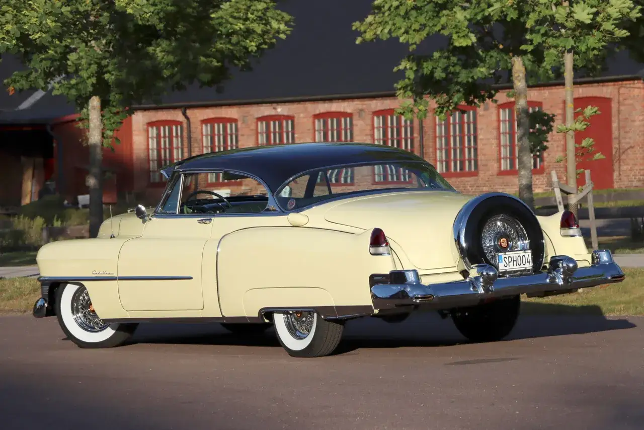 En gul gammal amerikansk bil, en Cadillac, parkerad framf&ouml;r en r&ouml;d tegelbyggnad med gr&ouml;na tr&auml;d.