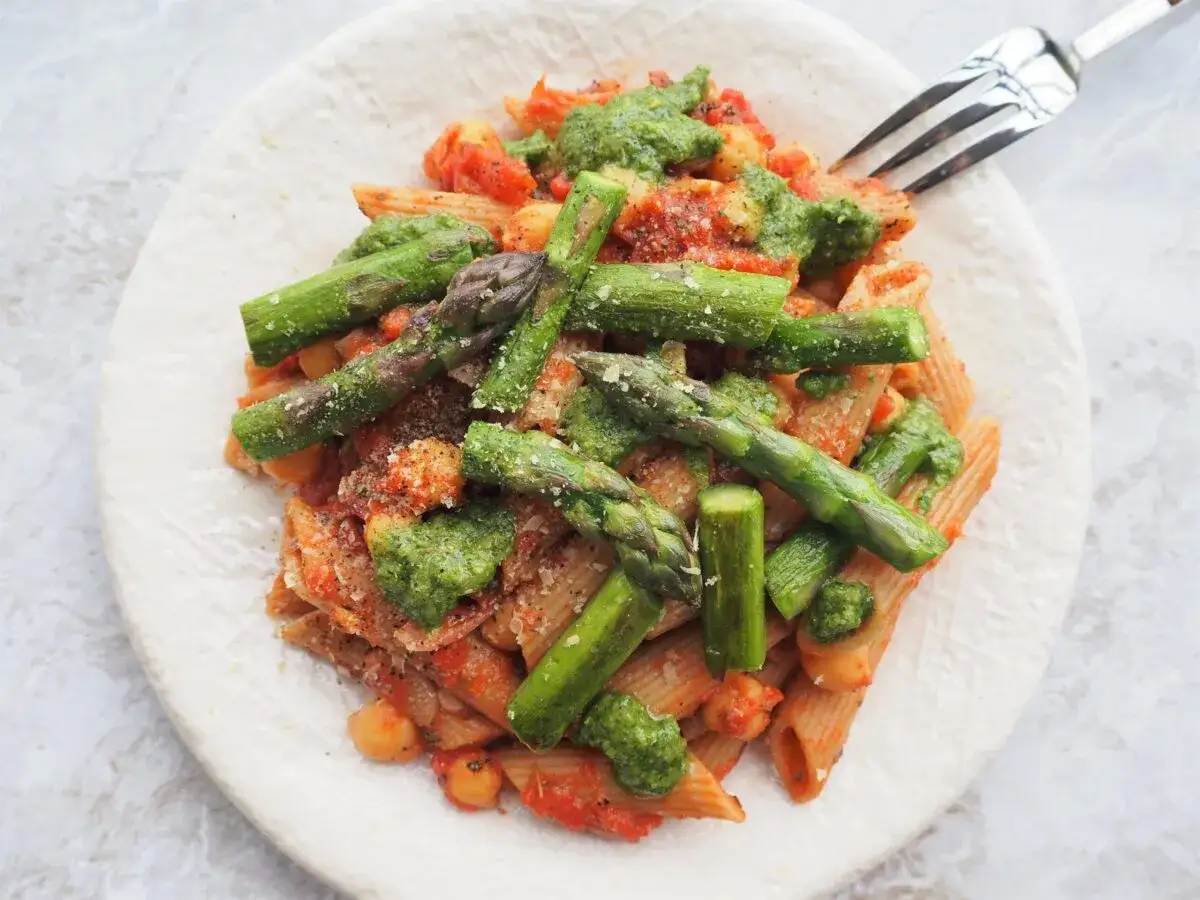 Pyszne makaron ze szparagami i pomidorami, polany zielonym pesto, posypany parmezanem. Idealne danie na wiosnę.