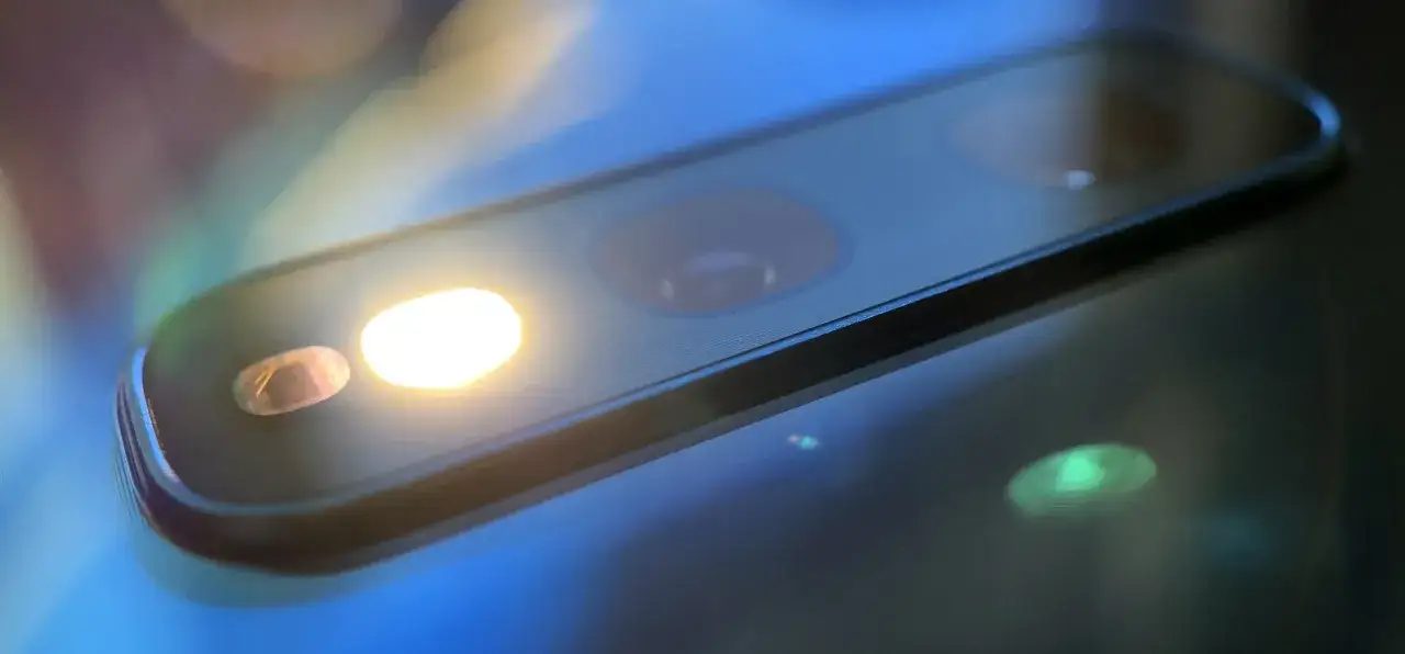 Jasne światło z latarki w telefonie oświetla obiektyw aparatu, tworząc refleksy.