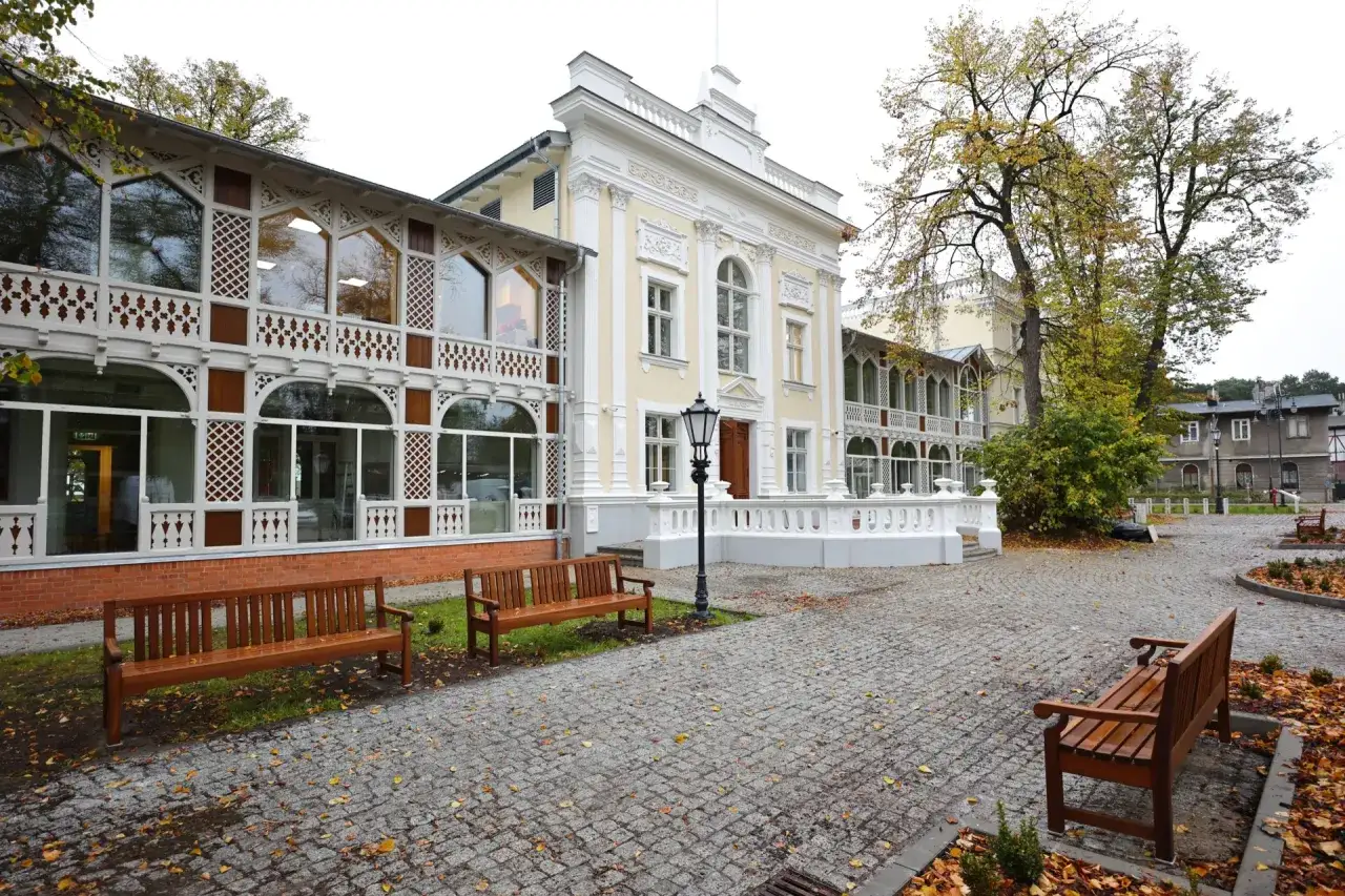 Elegancki budynek z werandą, przypominający dom zdrojowy w Hevelianum, otoczony jesiennymi liśćmi i ławkami.