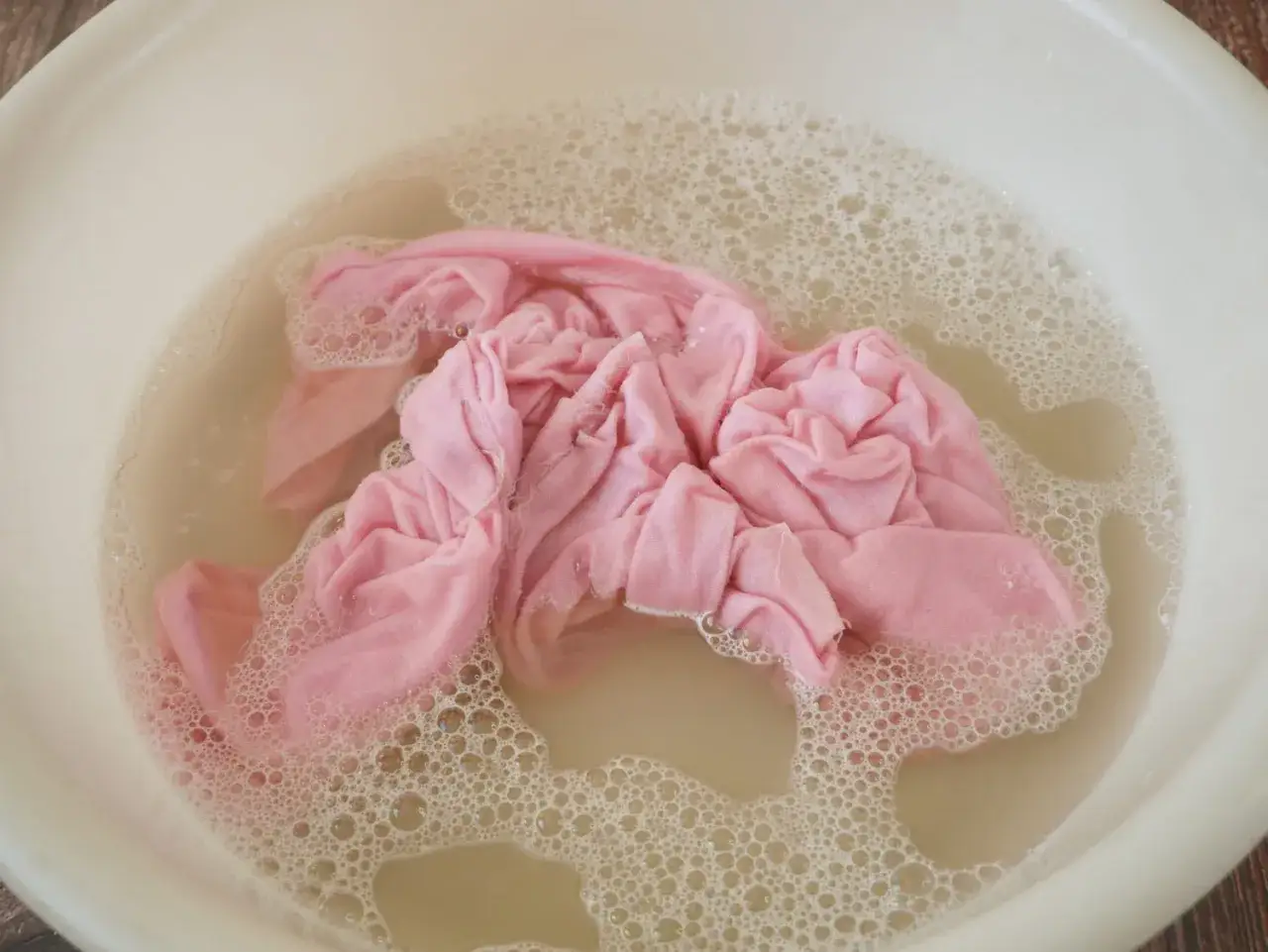 Un linge d&eacute;teint rose trempe dans l'eau savonneuse. Une astuce grand-m&egrave;re pour raviver les couleurs.