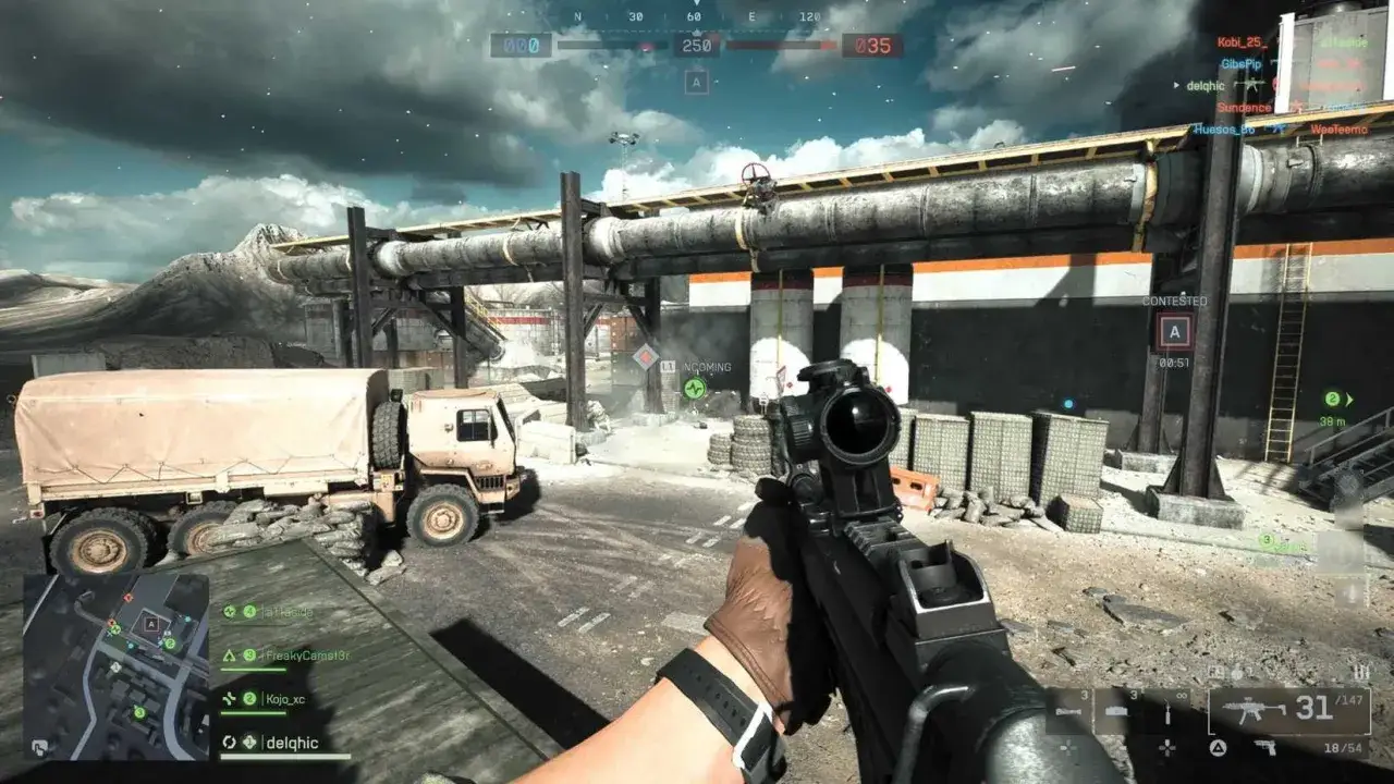 Gracz celuje z karabinu na polu bitwy w grze Battlefield 6. W tle ciężarówka i przemysłowa konstrukcja.