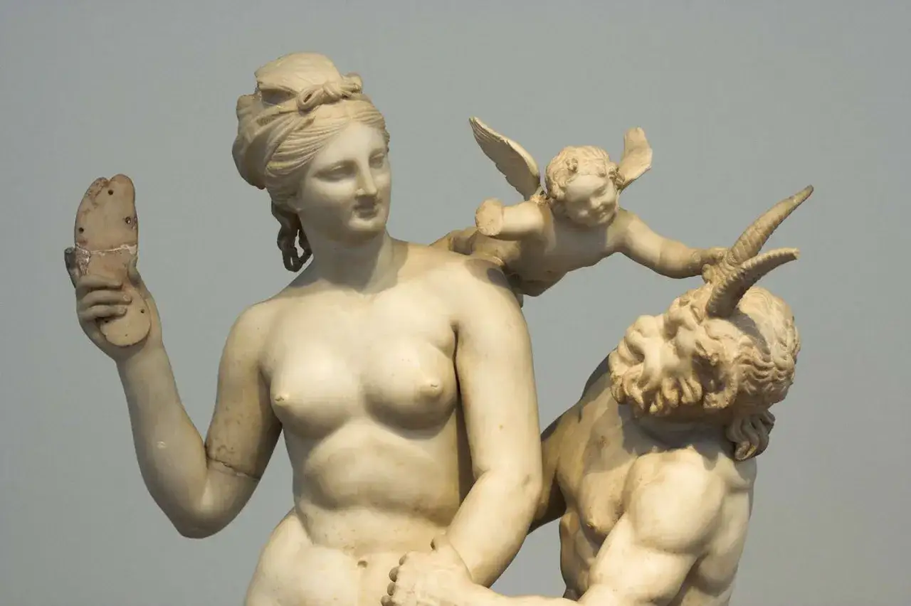 Sculpture d'Aphrodite, tenant une sandale, avec un amour ailé sur son épaule et un satyre aux cornes recourbées. Une scène de l'aphrodite histoire.