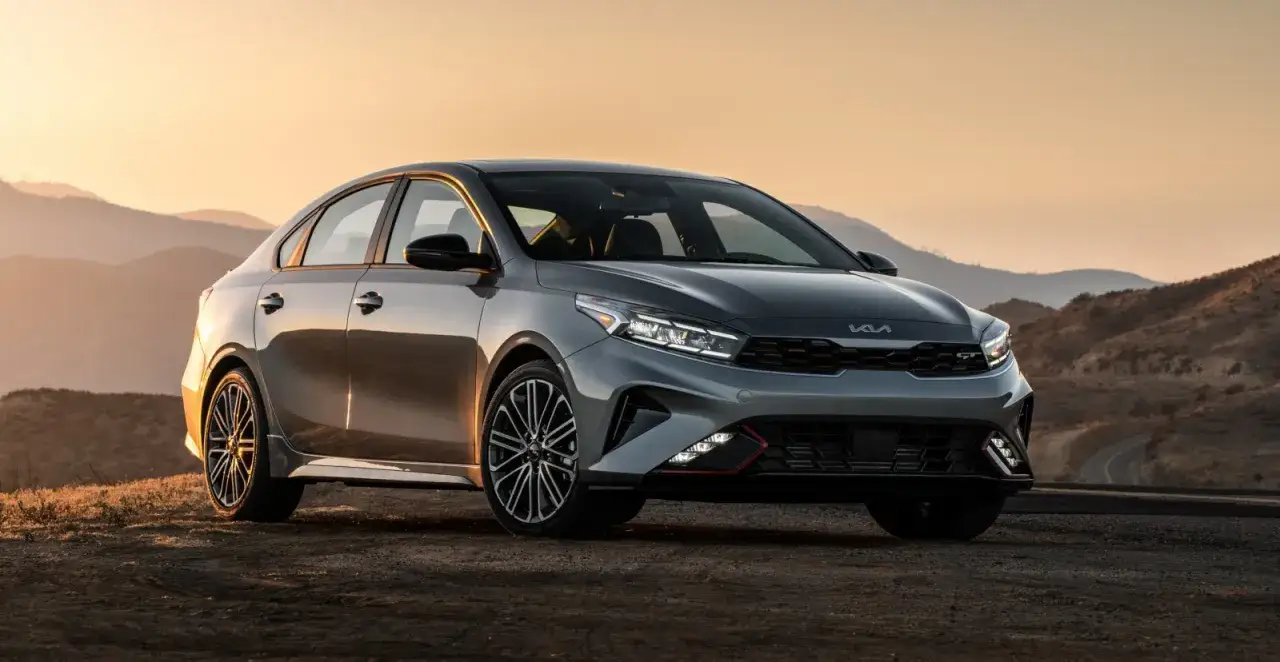 Szary Kia Forte GT na tle zachodzącego słońca i górskich krajobrazów.