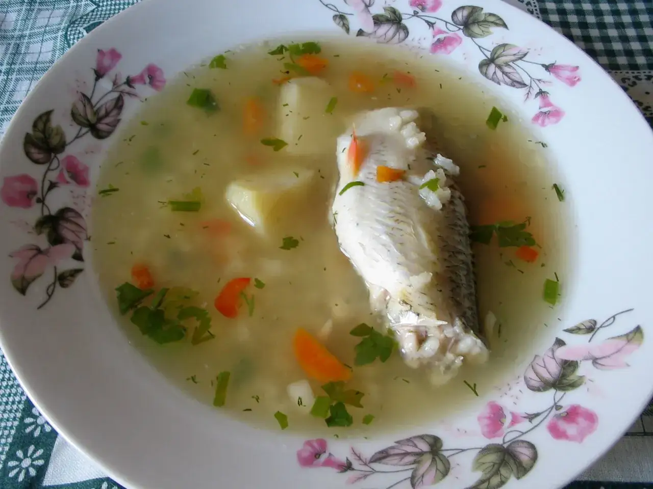 Aromatyczna rosyjska zupa rybna z kawałkiem ryby, ziemniakami, marchewką i zieloną pietruszką na talerzu z kwiatowym wzorem.