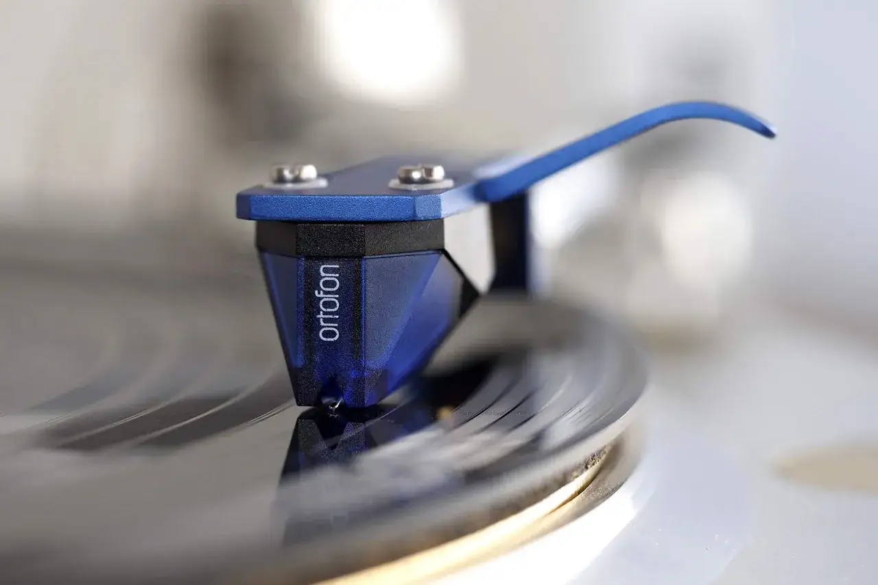 Nahaufnahme eines blauen Ortofon 2M Blue Tonabnehmers, der auf einer Vinylplatte für einen Test gleitet.