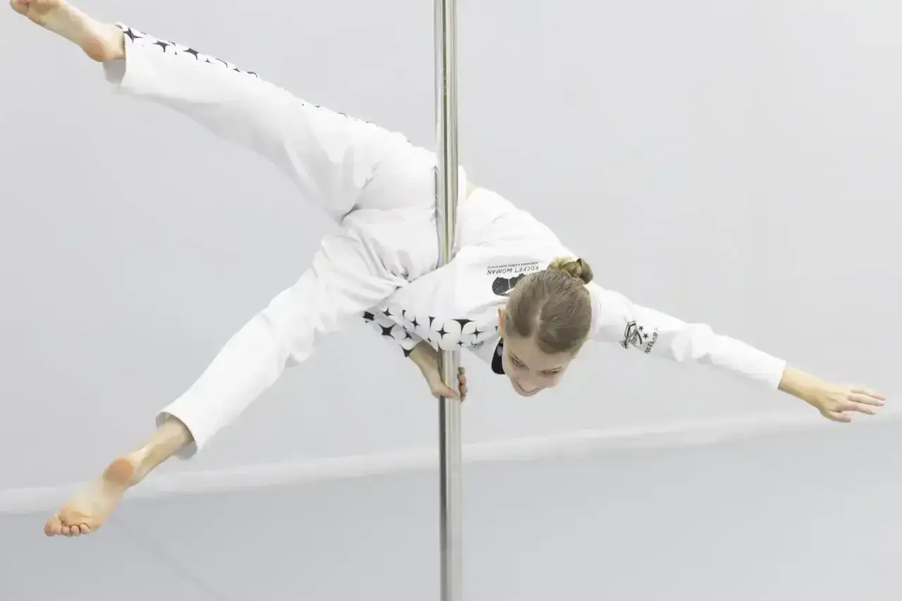 Dziewczyna w stroju do tańca na rurze, wykonująca akrobatyczną figurę. To imponujący pole dance sport.
