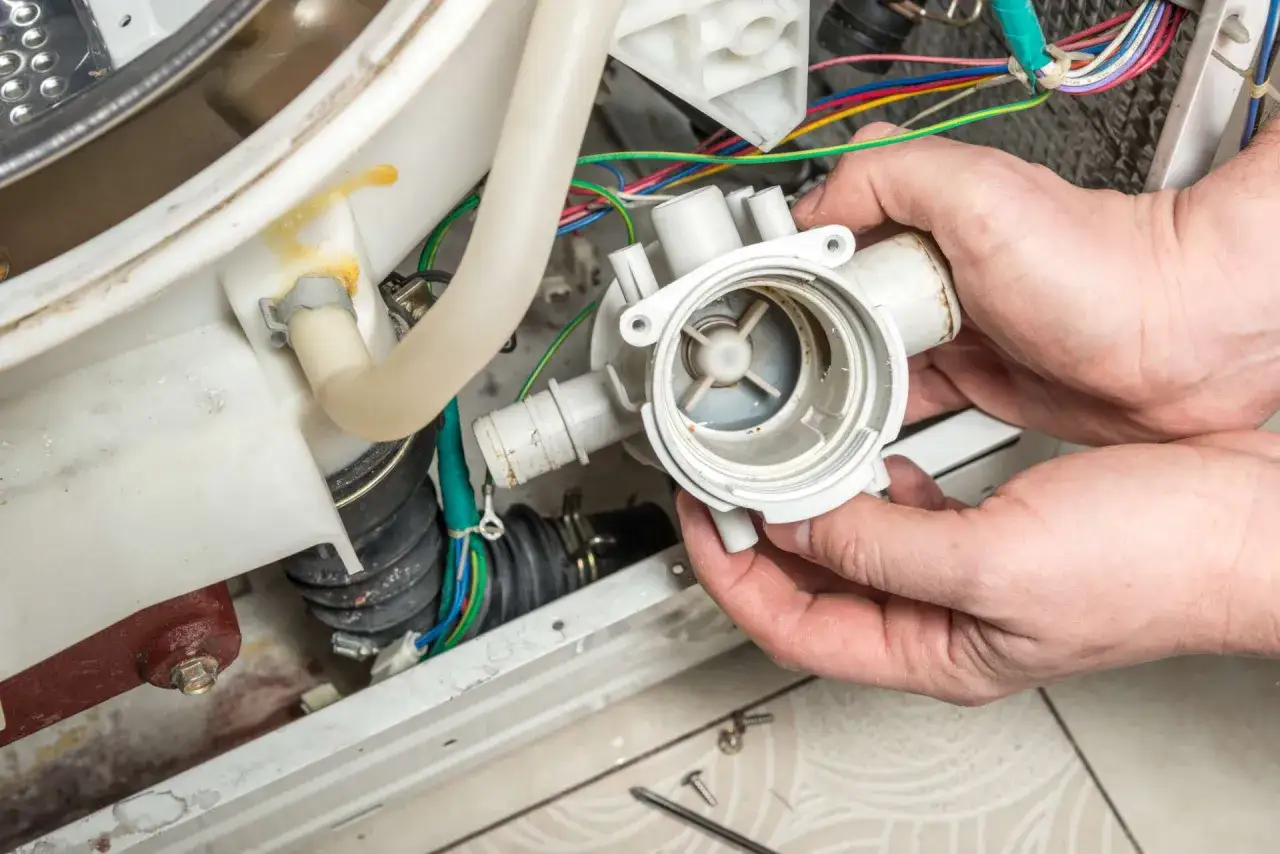 Hände halten eine Waschmaschine-Pumpe, die nicht abpumpt. Kabel und Schläuche sind sichtbar.