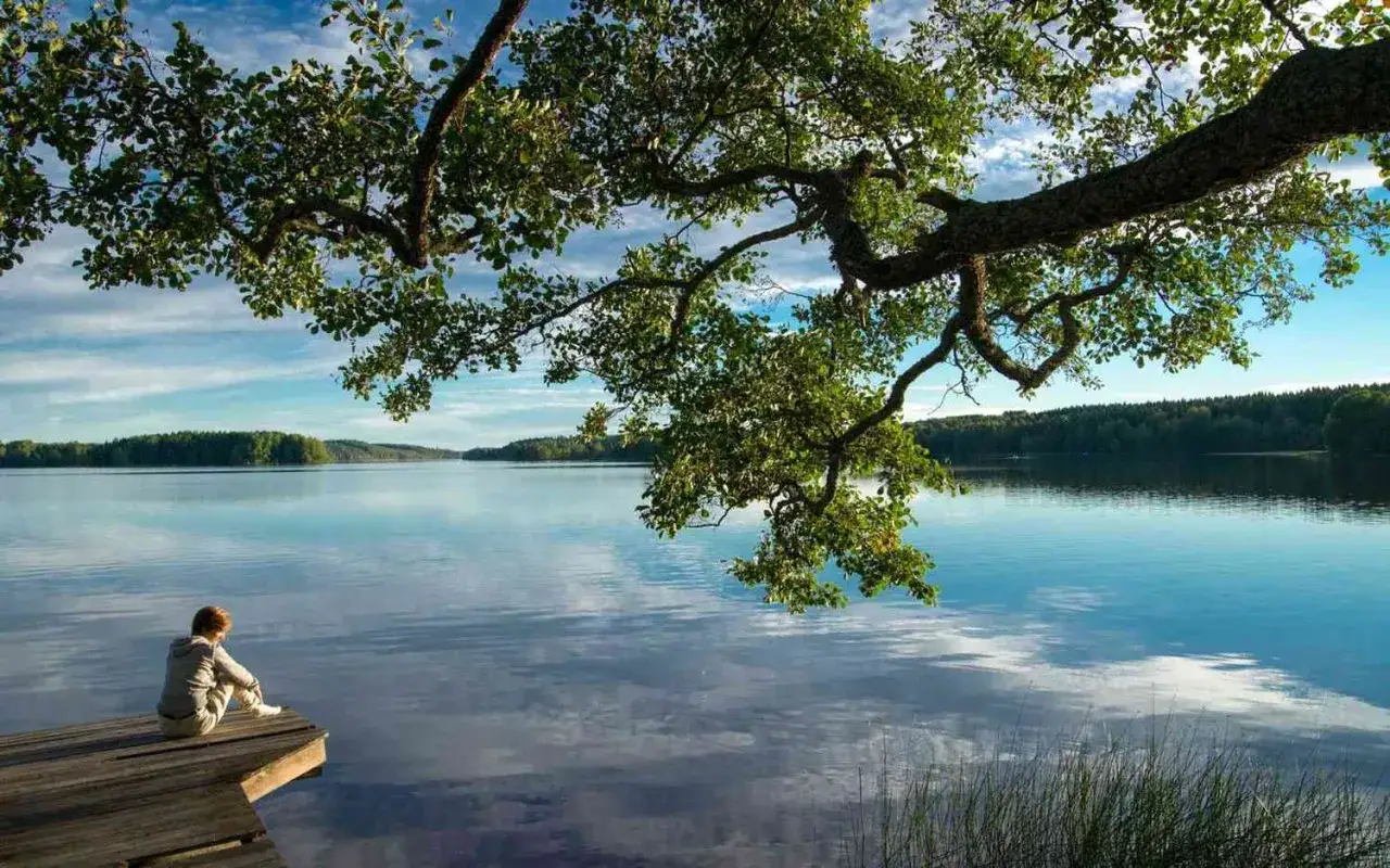 Lugn person sitter på brygga vid en stilla sjö, perfekt för ett yoga retreat i svensk natur.