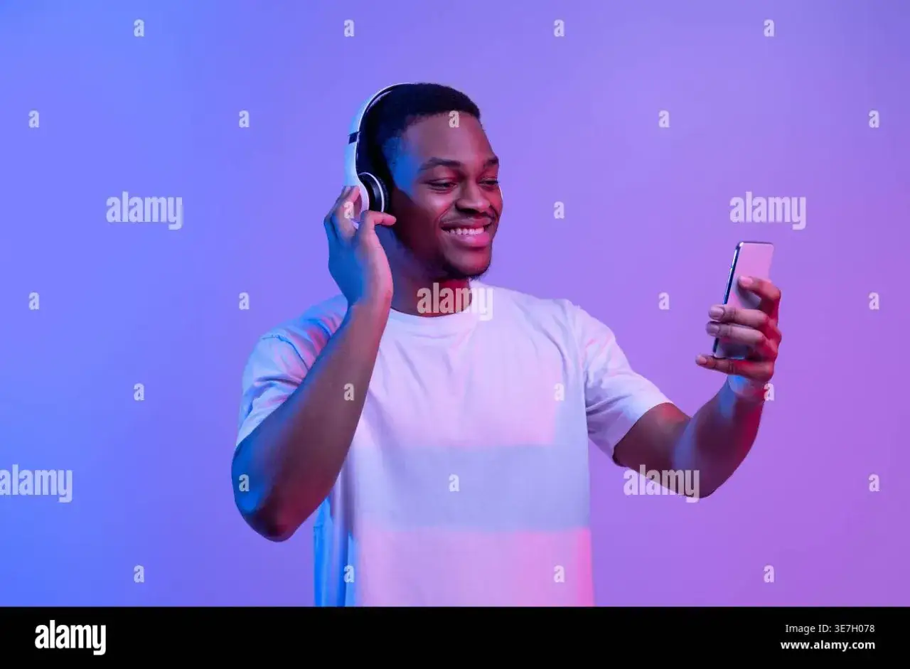 Uśmiechnięty mężczyzna w słuchawkach cieszy się streamingiem muzyki na telefonie.