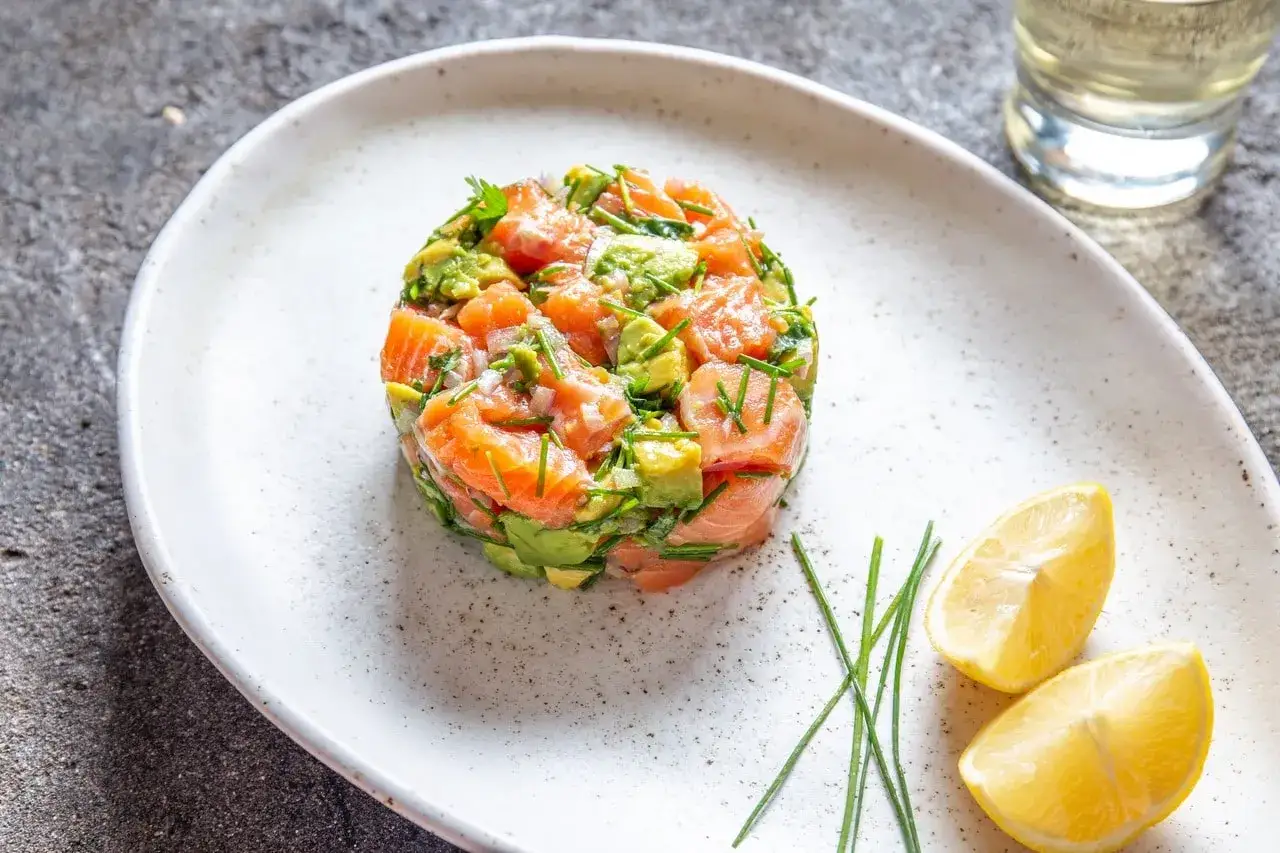 Delicioso tartar de salm&oacute;n y aguacate, fresco y vibrante, servido con gajos de lim&oacute;n y cebollino.