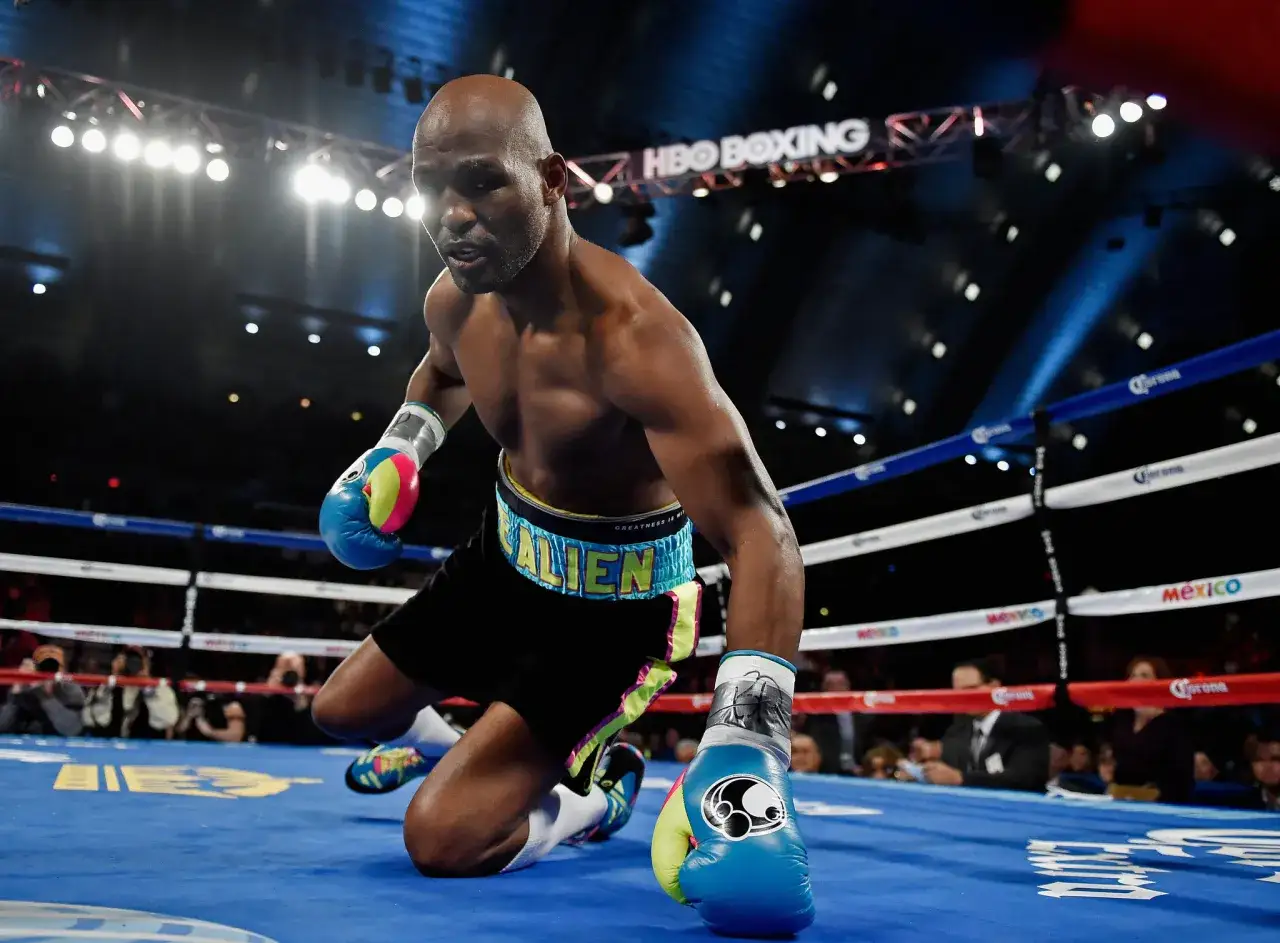 A determined Hopkins boxer kneels in the ring, his colorful gloves and shorts a stark contrast to the dark arena.