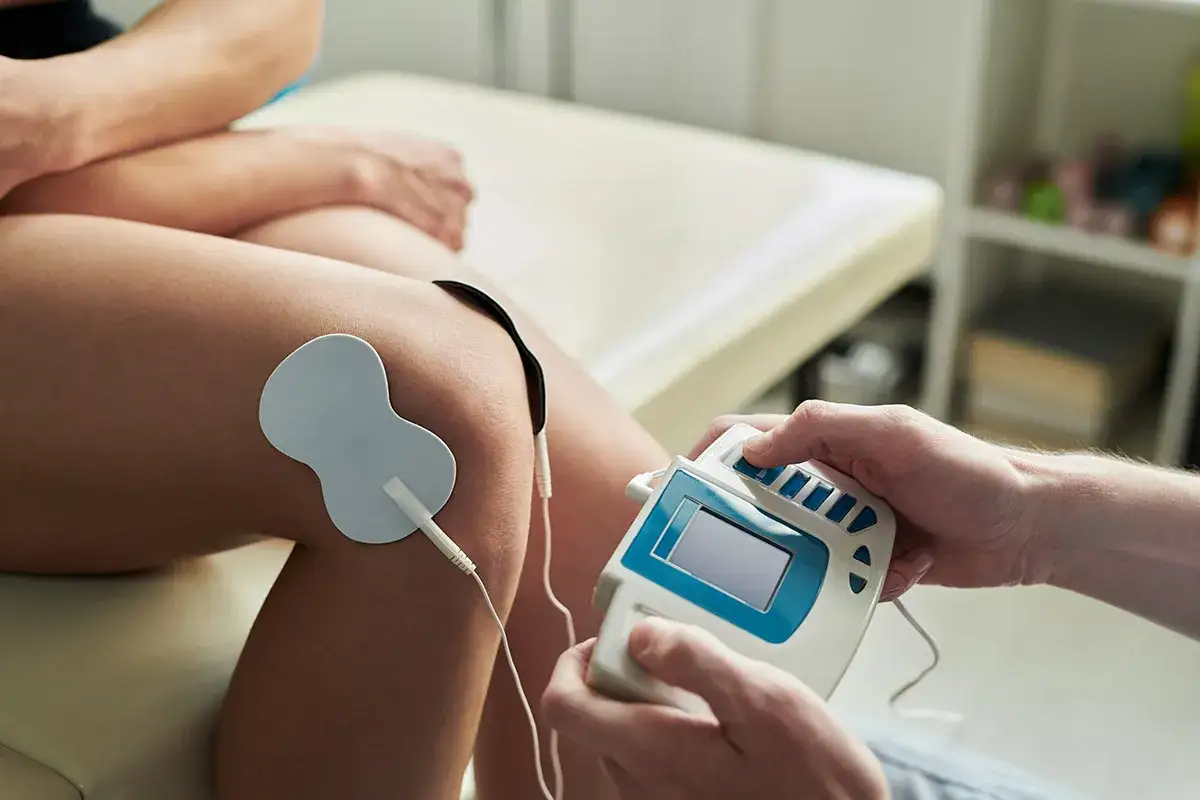 Elektrostymulacja TENS na kolanie. Fizjoterapeuta reguluje urządzenie, minimalizując potencjalne prądy TENS skutki uboczne.