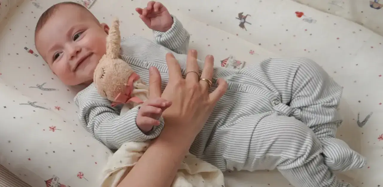 Uroczy niemowlak w pajacyku leży w łóżeczku. Mama delikatnie głaszcze go po brzuszku, pokazując, jak ubrac dziecko do spania.