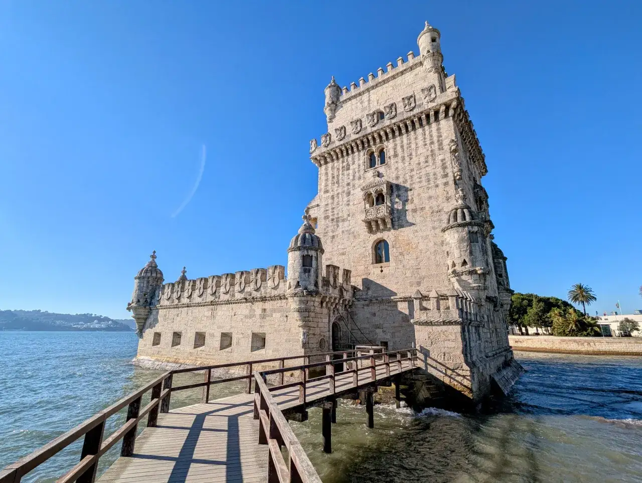 Torre de Bel&eacute;m, ein Wahrzeichen Portugals, ragt majest&auml;tisch aus dem Wasser. Eine Holzbr&uuml;cke f&uuml;hrt zum steinernen Bauwerk.