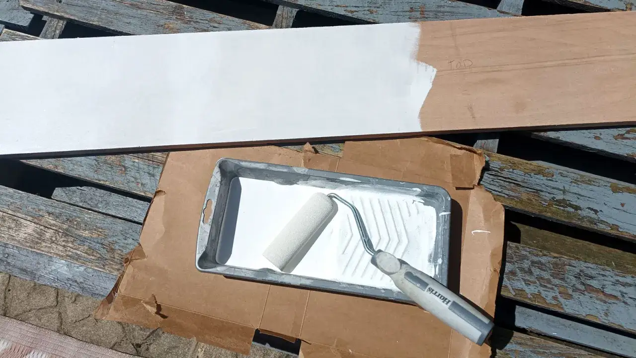 Un rouleau de peinture blanche est prêt à peindre un panneau de contreplaqué sur des planches de bois usées.