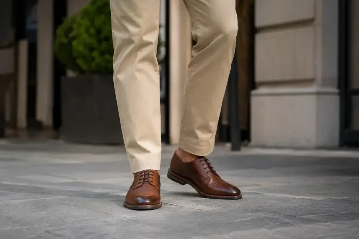 Eleganckie buty męskie w odcieniu kolor koniakowy, zestawione z beżowymi spodniami, prezentują się stylowo na miejskim bruku.