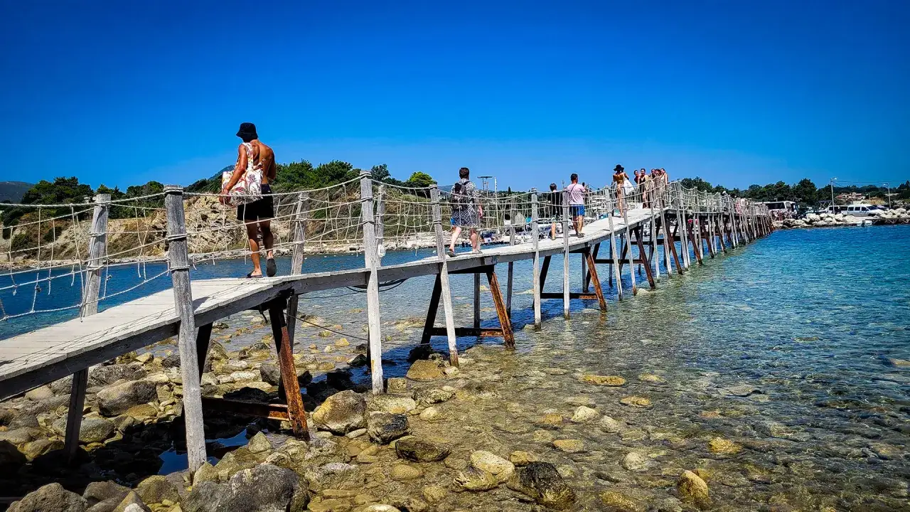 Drewniany mostek prowadzi na Cameo Island. Ludzie spacerują po nim nad krystalicznie czystą wodą.