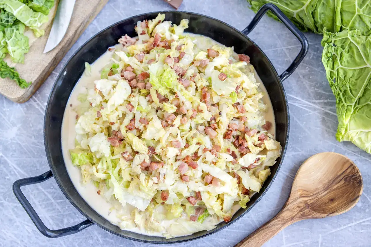 Herzhafte Wirsing-Rezepte: Cremiger Wirsing mit Speck in einer Pfanne, daneben ein Messer und frischer Wirsing.