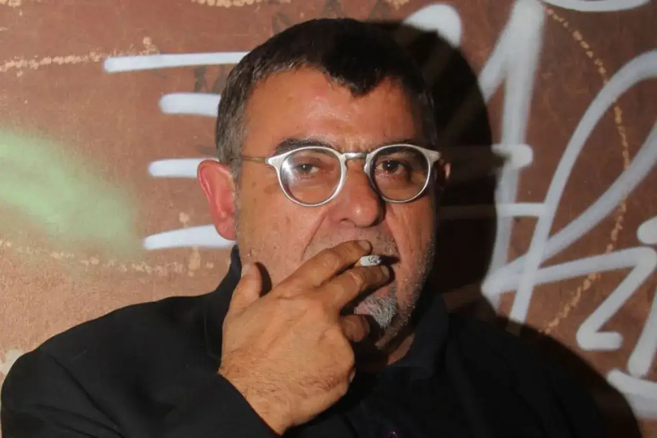 Giancarlo Cauteruccio, con occhiali e sigaretta, posa davanti a un muro con graffiti.