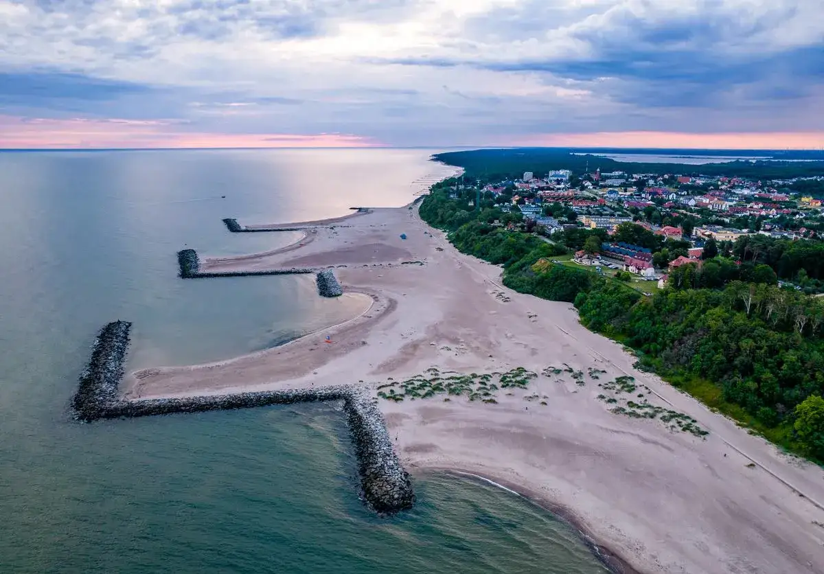 Zachód słońca nad Bałtykiem, falochrony tworzą malownicze zatoczki na plaży. Miasto nad morzem, jak polski Dubaj, w blasku ostatnich promieni.