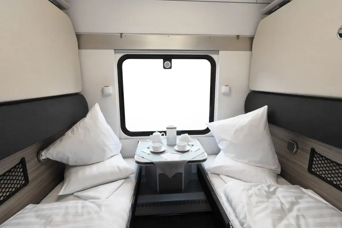 Gemütliche Schlafkabine für die Reise von Hamburg nach Zürich. Zwei Betten mit weißen Kissen und Decken, ein Tisch mit Tee-Service vor dem Fenster.