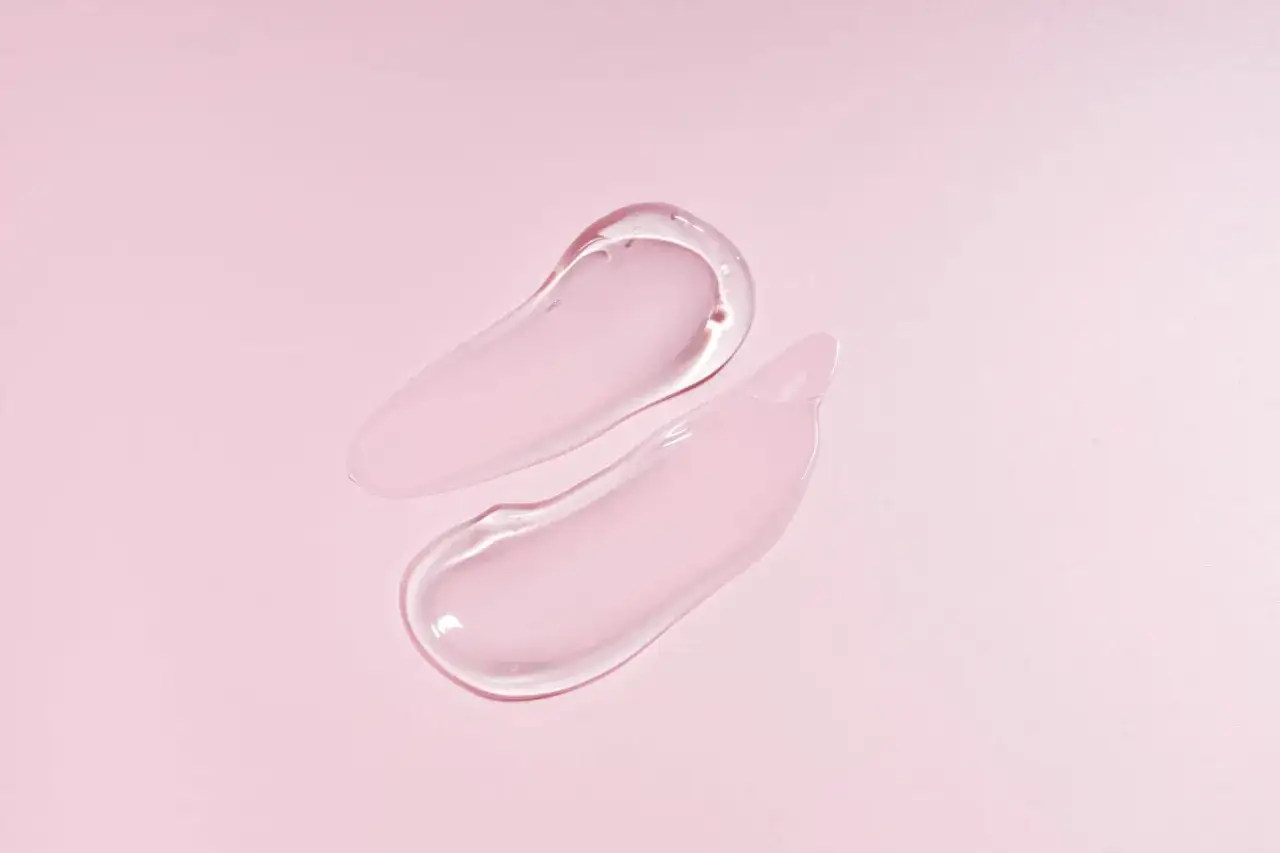 Två kladdar av genomskinlig gel med en svag rosa ton på en ljusrosa bakgrund. Glycerin i hudvård ger fukt.
