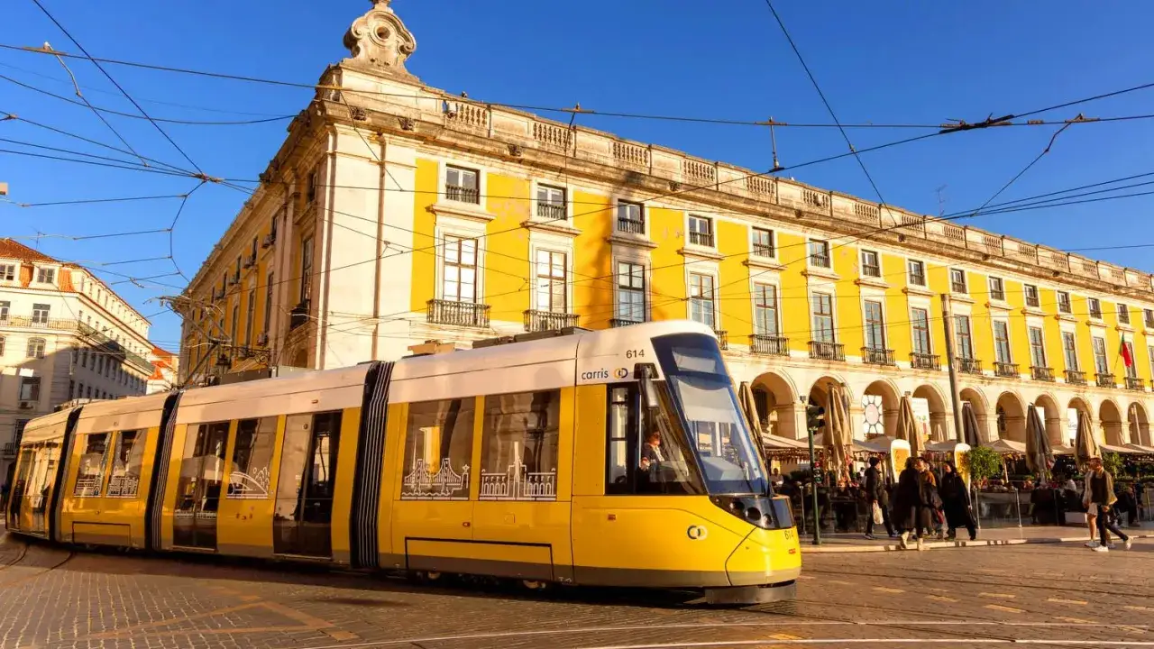 Gelbe stra&szlig;enbahn lissabon f&auml;hrt vorbei an einem gelben Geb&auml;ude mit Arkaden.