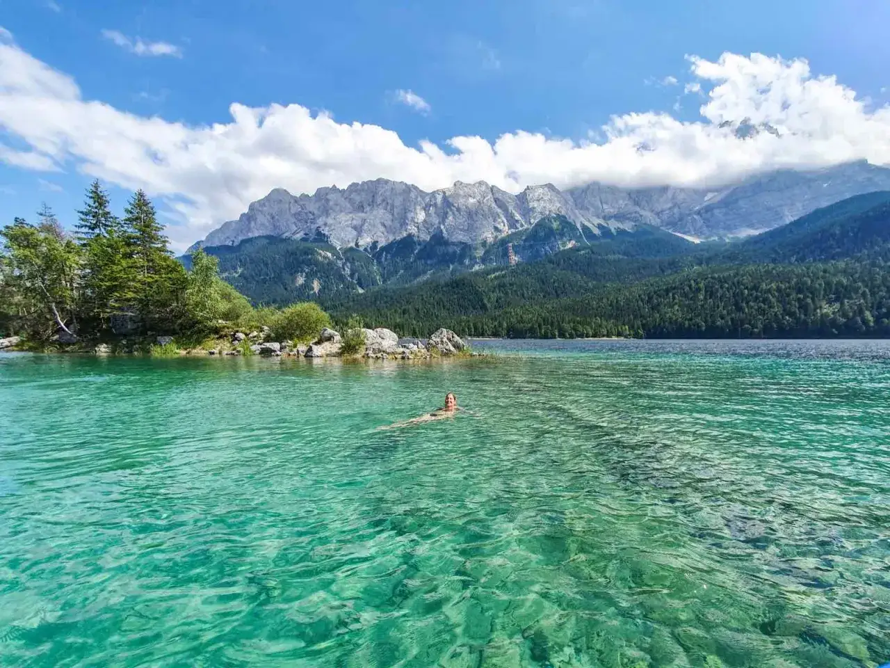 Eine Person schwimmt im kristallklaren Wasser des Eibsees, umgeben von gr&uuml;nen W&auml;ldern und majest&auml;tischen Bergen. Der Eibsee Rundweg l&auml;dt zu solchen Erlebnissen ein.