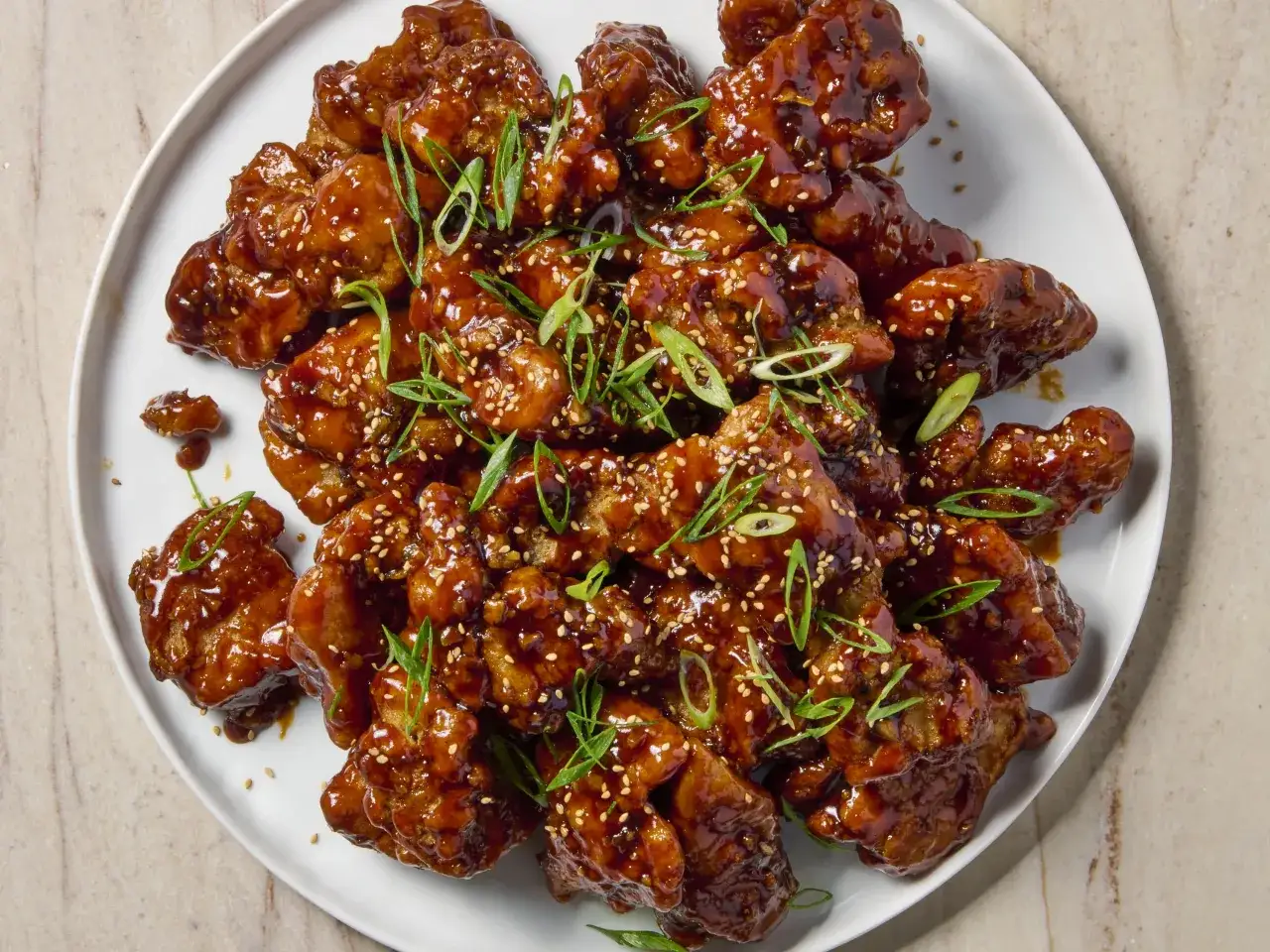 En stor portion krispig koreansk kyckling täckt i en glansig, söt och kryddig sås, toppad med sesamfrön och färsk salladslök.